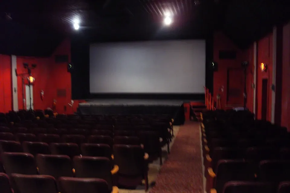 Rows of dark red seats in a small, dimly lit theatre facing a blank screen and stage