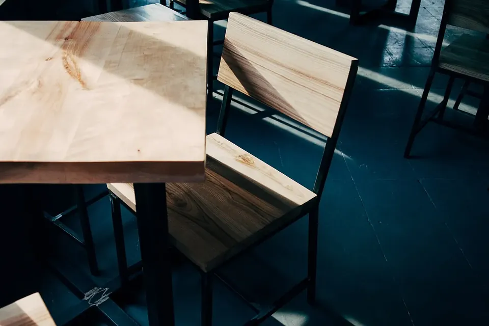 A pale wooden table and two matching wooden chairs in a dim room with a dark blue floor