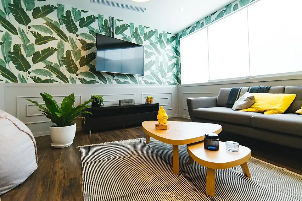 The lounge of a shared workspace with a grey sofa, low wooden tables, plants and leaf-patterned wallpaper