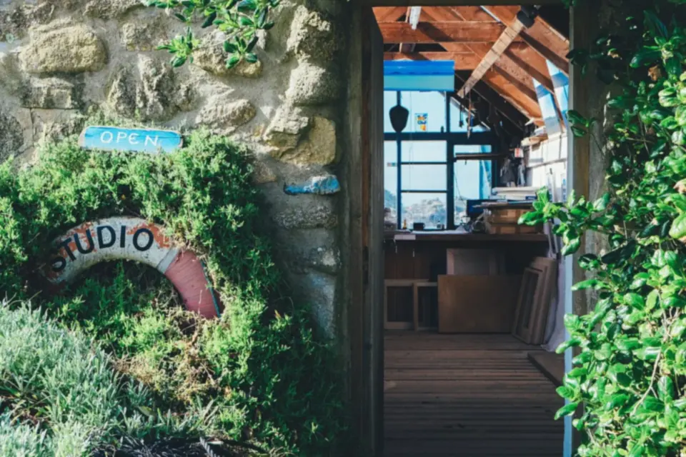 An open wooden door in an old stone wall overgrown with plants, with a painted Studio sign and a small Open sign